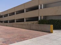 a parking garage with two entrances and a red brick sidewalk with some bushes on the side