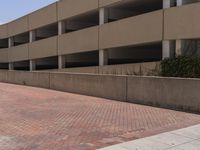 a parking garage with two entrances and a red brick sidewalk with some bushes on the side