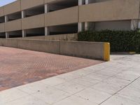 a parking garage with two entrances and a red brick sidewalk with some bushes on the side