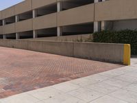 a parking garage with two entrances and a red brick sidewalk with some bushes on the side