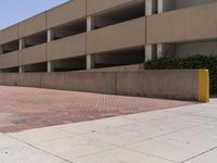 a parking garage with two entrances and a red brick sidewalk with some bushes on the side