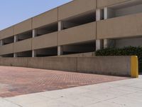 a parking garage with two entrances and a red brick sidewalk with some bushes on the side