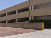 a parking garage with two entrances and a red brick sidewalk with some bushes on the side