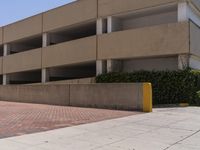 a parking garage with two entrances and a red brick sidewalk with some bushes on the side