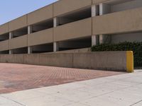 a parking garage with two entrances and a red brick sidewalk with some bushes on the side