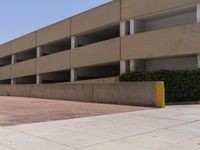 a parking garage with two entrances and a red brick sidewalk with some bushes on the side