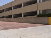 a parking garage with two entrances and a red brick sidewalk with some bushes on the side