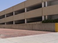 a parking garage with two entrances and a red brick sidewalk with some bushes on the side