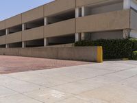 a parking garage with two entrances and a red brick sidewalk with some bushes on the side