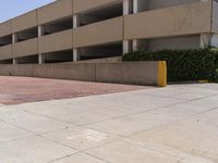 a parking garage with two entrances and a red brick sidewalk with some bushes on the side