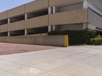 a parking garage with two entrances and a red brick sidewalk with some bushes on the side