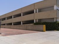 a parking garage with two entrances and a red brick sidewalk with some bushes on the side