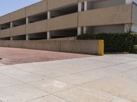 a parking garage with two entrances and a red brick sidewalk with some bushes on the side