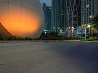 a woman walks past an orange sphere building, with palm trees nearby, in a city