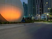 a woman walks past an orange sphere building, with palm trees nearby, in a city