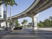 a very busy street with a bridge over it that is both tall and wide, with cars and palm trees in the background