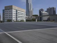 a wide empty parking lot in front of a tall office building with a bridge overhead