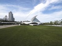 a large white structure is in the grass of the lawn in front of buildings and water