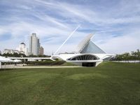 a large white structure is in the grass of the lawn in front of buildings and water