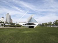 a large white structure is in the grass of the lawn in front of buildings and water