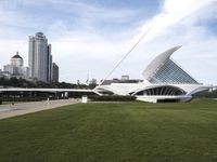 a large white structure is in the grass of the lawn in front of buildings and water