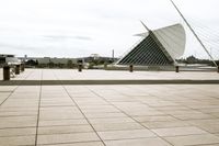 a long, wide white sculpture in front of some buildings on a river bank with water and sky