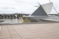 a long, wide white sculpture in front of some buildings on a river bank with water and sky