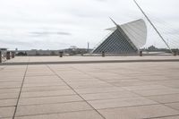 a long, wide white sculpture in front of some buildings on a river bank with water and sky