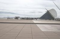 a long, wide white sculpture in front of some buildings on a river bank with water and sky