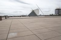 a long, wide white sculpture in front of some buildings on a river bank with water and sky