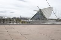 a long, wide white sculpture in front of some buildings on a river bank with water and sky