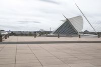 a long, wide white sculpture in front of some buildings on a river bank with water and sky