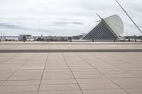 a long, wide white sculpture in front of some buildings on a river bank with water and sky