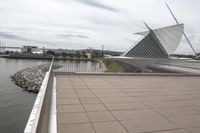 a long, wide white sculpture in front of some buildings on a river bank with water and sky