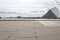 a long, wide white sculpture in front of some buildings on a river bank with water and sky