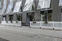 an open window store with a picketer fence on the sidewalk in front of it