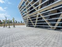 the building with windows is located near a sidewalk near a park with some trees and bushes