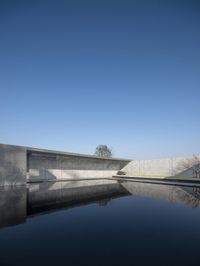 large concrete building with water reflecting on the ground and side in front of it, and a man standing next to the water area