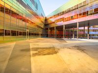 a building with several different colored glass walls surrounding it that has an open street and walkway near the entrance