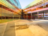 a building with several different colored glass walls surrounding it that has an open street and walkway near the entrance