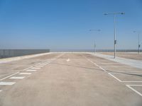 empty parking lot next to a fence and light posts, with empty road signs in it