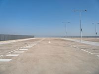 empty parking lot next to a fence and light posts, with empty road signs in it