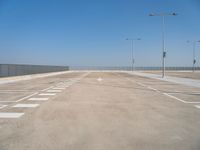 empty parking lot next to a fence and light posts, with empty road signs in it