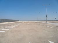 empty parking lot next to a fence and light posts, with empty road signs in it