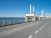 an empty highway with several pipe - like chimneys near the oceanfront and a large structure in the middle