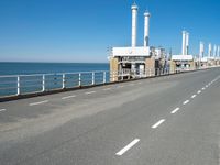 an empty highway with several pipe - like chimneys near the oceanfront and a large structure in the middle