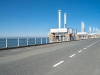 an empty highway with several pipe - like chimneys near the oceanfront and a large structure in the middle