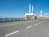 an empty highway with several pipe - like chimneys near the oceanfront and a large structure in the middle