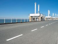 an empty highway with several pipe - like chimneys near the oceanfront and a large structure in the middle