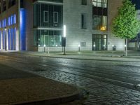 a street corner in the evening with a city building lit up and a street light that is shining blue